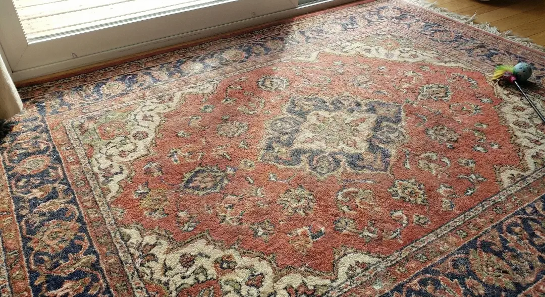 Photo of a vintage carpet in the eastern style with a red-blue color, in the summer The wool is placed on the wooden top of the window, with the cat toy in the corner.