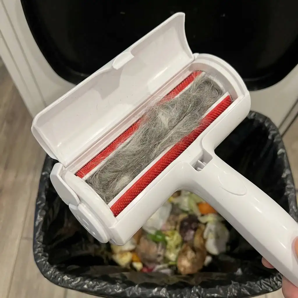 Open kitchen trash can storage chamber filled with a dense bundle of grey and white pet fur. Open kitchen trash can storage chamber filled with a dense bundle of grey and white pet fur.